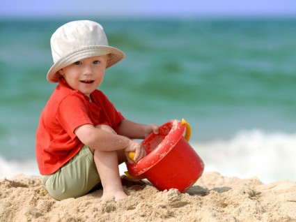 мальчик сидит на песке и держит в руке ведерко