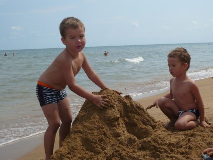 Мальчики-двойняшки строят на пляже замок из песка