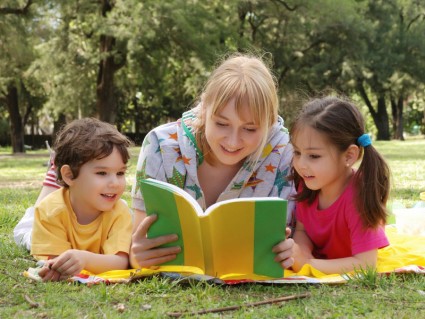 Девушка читает жёлто-зеленую книгу двум детям