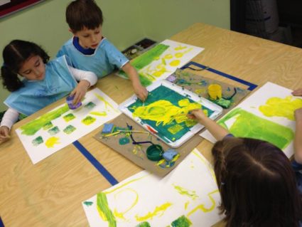 3 детей, 2 в синих фартуках рисуют в зелёно-жёлтой гамме
