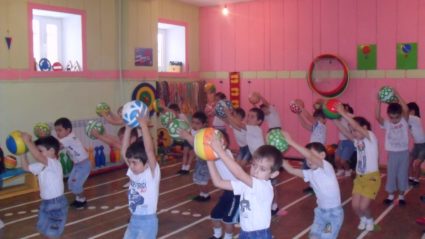 Дети с мячами над головой на занятии физкультутрой