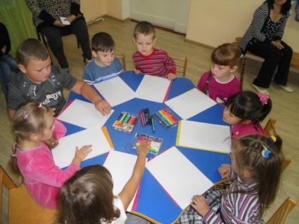 Дети сидят за круглым столом, перед ними листы А4 и фломастеры