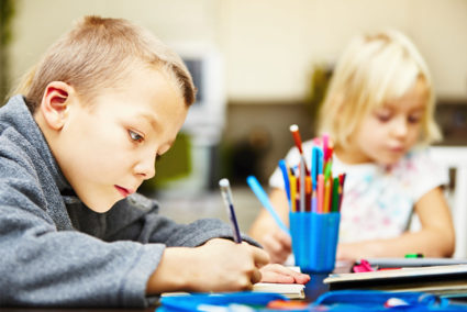 Мальчик и девочка садят за партой и рисуют карандашами