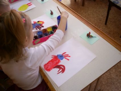 Девочка рисует красками красного петушка