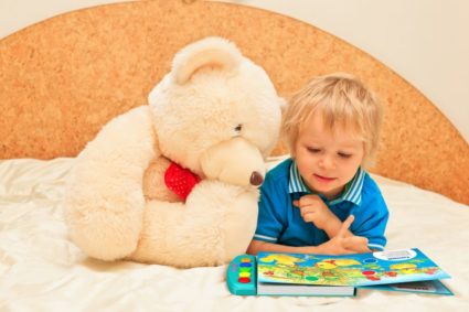 Ребёнок рассматривает книжку, рядом плюшевый медведь